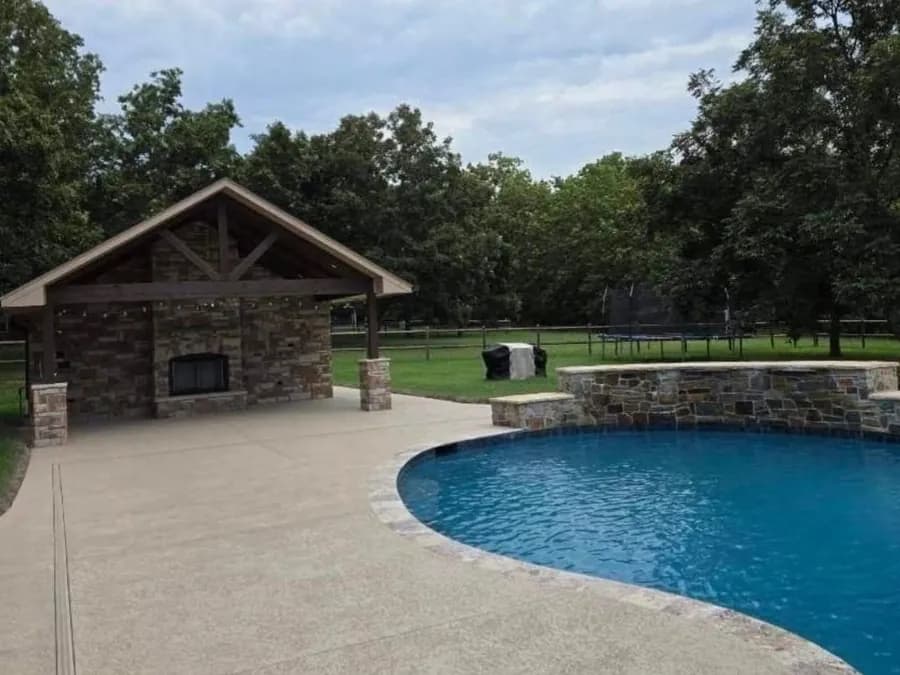 Freeform gunite pool beside a stone pavilion by Anthem Pools