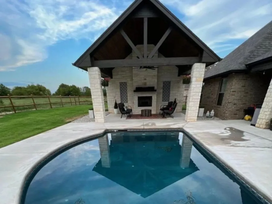 Stone pavilion with an outdoor fireplace beside a pool by Anthem Pools