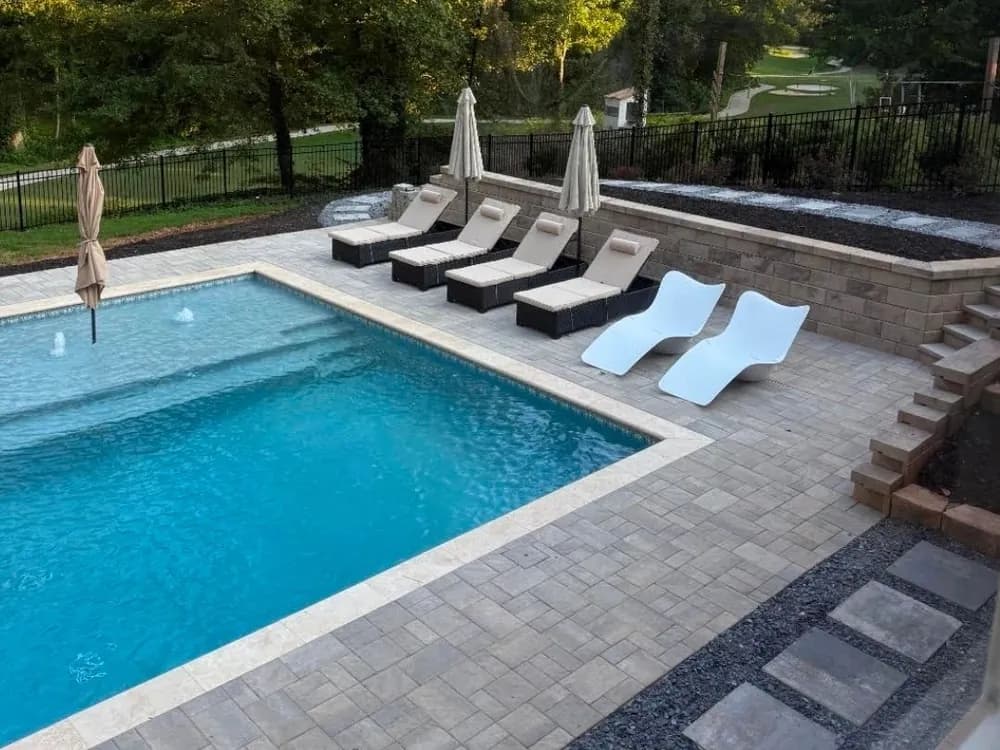 Pool with a sun shelf, loungers and a paver patio with retaining wall, built by Anthem Pools