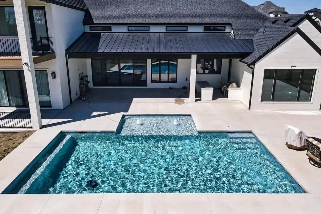 Geometric gunite pool with an attached spa behind a modern home, built by Anthem Pools